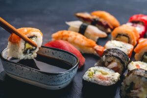 person-hold-sushi-maki-roll-with-chopstick-put-it-soy-sauce-oriental-japanese-healthy-cuisine-scaled
